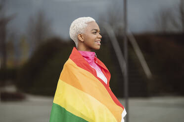 Lächelnde LGBTQIA-Frau in Regenbogenfahne gehüllt - JCCMF05143