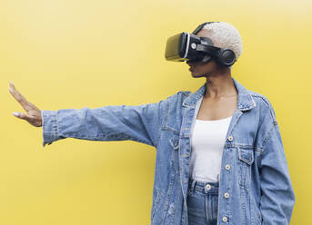 Young woman with virtual reality headset against yellow background - JCCMF05148