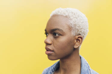 Contemplative woman with short blond hair against yellow background - JCCMF05153