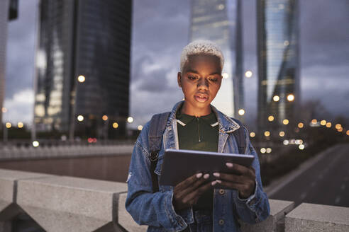 Frau mit Tablet-PC steht auf einer Brücke in der Stadt in der Abenddämmerung - JCCMF05191