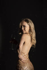 Young woman in golden sequin cocktail dress with hand on hip against black background - SSGF00431