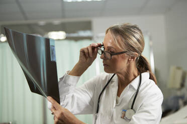 Female doctor holding eyeglasses examining X-ray in medical room - PMF02122