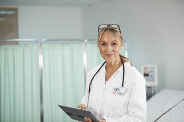 Smiling doctor holding tablet PC in medical room - PMF02123