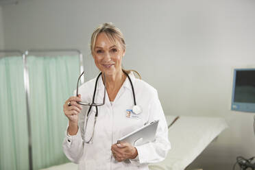 Smiling doctor with eyeglasses holding tablet PC in medical room - PMF02124