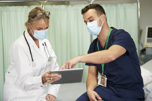 Krankenpfleger mit Gesichtsschutzmaske erklärt Arzt über Tablet-PC in medizinischem Raum - PMF02130