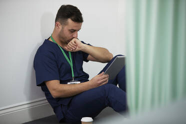Mitarbeiter des Gesundheitswesens schaut auf einen Tablet-PC, der in einem medizinischen Raum an der Wand steht - PMF02137