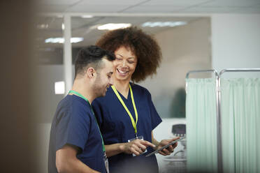 Lächelnde Krankenschwester mit Tablet-PC, die einen Kollegen im Krankenzimmer beobachtet - PMF02140