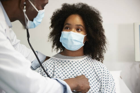 Arzt untersucht einen Patienten mit Gesichtsschutzmaske im Krankenhaus - PMF02164