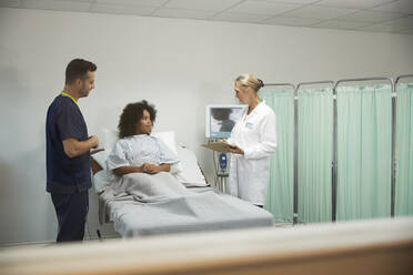 Arzt und Krankenschwester besprechen sich mit einem Patienten im Krankenzimmer eines Krankenhauses - PMF02192