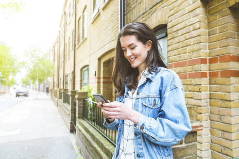 Schöne junge Frau vor einem Gebäude stehend, Textnachrichten auf einem Smartphone - WPEF05697