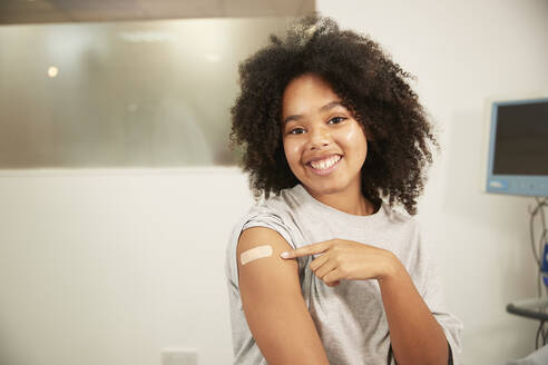 Lächelndes Mädchen, das auf einen geimpften Arm im Krankenhauszimmer zeigt - PMF02209