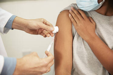 Doctor injecting COVID-19 vaccination to girl through syringe in medical room - PMF02210