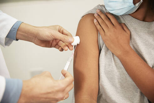 Ein Arzt injiziert einem Mädchen die COVID-19-Impfung mit einer Spritze im Behandlungsraum - PMF02210