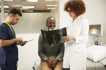 Doctor discussing X-ray with patient by nurse using tablet PC in medical room - PMF02214