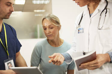 Ein älterer Patient schaut auf einen Tablet-PC, der von medizinischem Personal im Behandlungsraum bedient wird - PMF02222