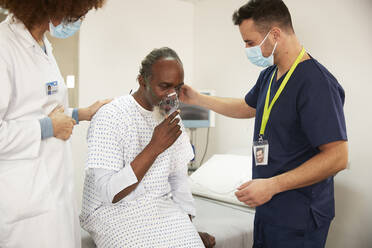Mitarbeiter des Gesundheitswesens trösten einen Patienten mit Sauerstoffmaske im Krankenzimmer - PMF02231