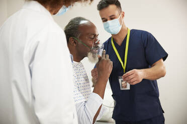 Patientin passt Sauerstoffmaske zusammen mit Gesundheitsexperten im medizinischen Raum an - PMF02234