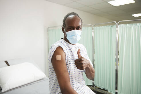 Patient mit geimpftem Arm, der im Behandlungszimmer den Daumen nach oben streckt - PMF02255