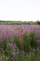 Young woman amidst pink flowering plants in meadow - SSGF00445