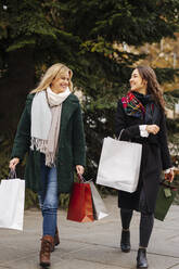 Lächelnde Frauen mit Einkaufstaschen, die sich auf dem Fußweg anschauen - DAWF02403