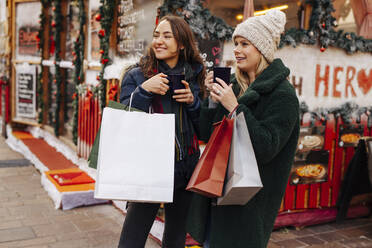 Frauen mit Einkaufstaschen genießen Glühwein auf dem Weihnachtsmarkt - DAWF02405