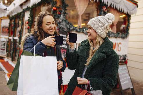 Lächelnde Frauen stoßen auf dem Weihnachtsmarkt mit einem Glühweinbecher an - DAWF02407