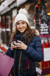 Junge Frau mit Strickmütze genießt Glühwein auf dem Weihnachtsmarkt - DAWF02417