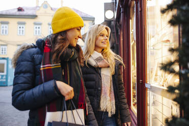 Friends looking through window of store at Christmas Market - DAWF02423