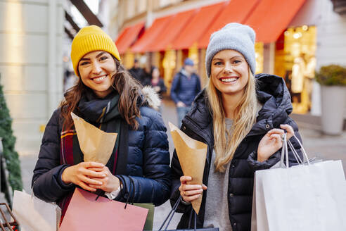 Lächelnde Frauen beim Einkaufen auf dem Weihnachtsmarkt mit Kastanien in Papiertüten - DAWF02429