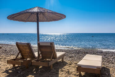 Leere Liegestühle am Küstenstrand mit klarer Linie des Horizonts über dem Meer im Hintergrund - MHF00561