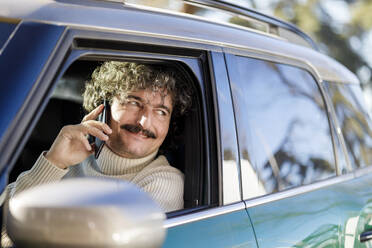 Smiling man talking on mobile phone looking out of car window - IFRF01366