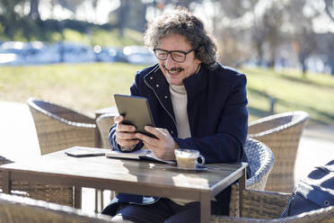 Glücklicher Mann bei einem Videogespräch mit Tablet-PC in einem Straßencafé - IFRF01371