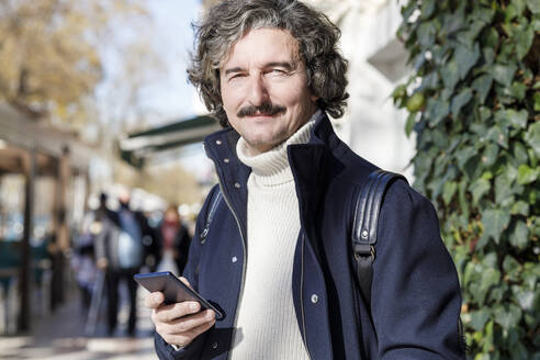 Smiling man holding smart phone on sunny day - IFRF01380