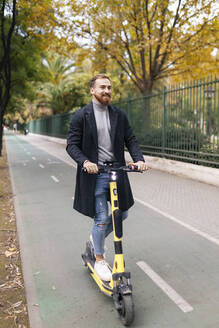 Happy man riding electric push scooter on bicycle lane - JRVF02428