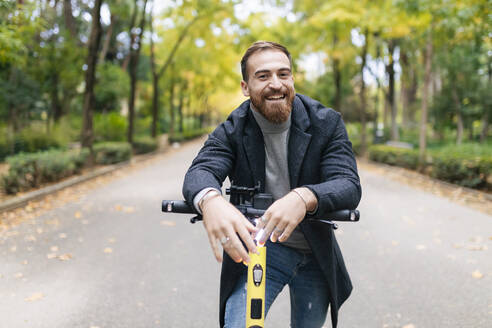 Happy bearded young man with e-scooter on road - JRVF02433