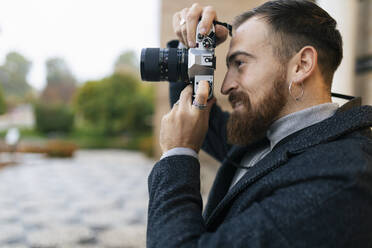 Young bearded man photographing through camera - JRVF02438