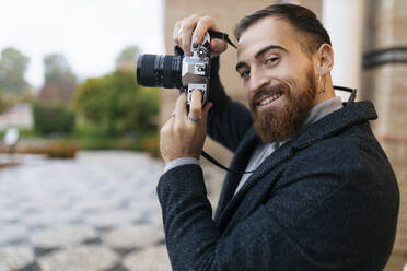 Smiling young bearded man with camera - JRVF02439