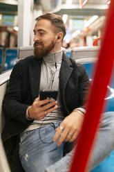 Junger Mann hört Musik mit In-Ear-Kopfhörern in der Straßenbahn - JRVF02453