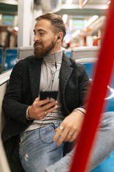 Young man listening music with in-ear headphones in tram - JRVF02453
