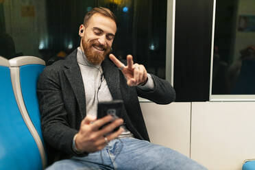 Mann macht Selfie mit Smartphone und Friedenszeichen in der Straßenbahn - JRVF02456