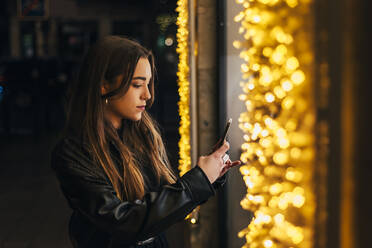 Junge Frau fotografiert nachts mit ihrem Smartphone - JRVF02476