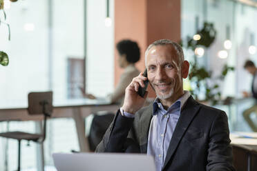 Smiling businessman talking on smart phone in office - EIF03059