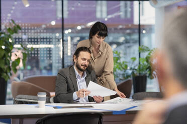 Businesswoman standing behind colleague examining paper document in office - EIF03064