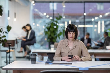 Geschäftsfrau, die im Büro eine SMS auf einem Smartphone schreibt - EIF03067