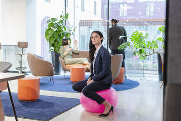 Selbstbewusste Geschäftsfrau, die auf einem Trichterball im Büro sitzt - EIF03079