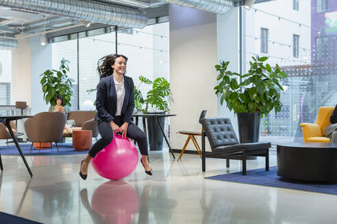 Verspielter junger Angestellter, der auf einem Hüpfball in der Büro-Lobby hüpft - EIF03080