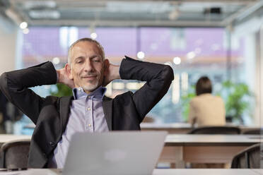 Businessman with hands behind head relaxing in office - EIF03094
