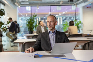 Lächelnder Geschäftsmann mit Laptop am Schreibtisch im Coworking Space - EIF03095