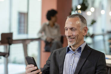 Lächelnder Geschäftsmann, der ein Smartphone im Büro benutzt - EIF03098