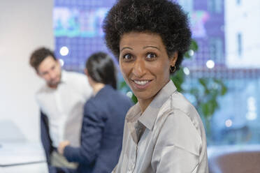 Lächelnde Geschäftsfrau mit Kollegen im Hintergrund im Coworking Space - EIF03105